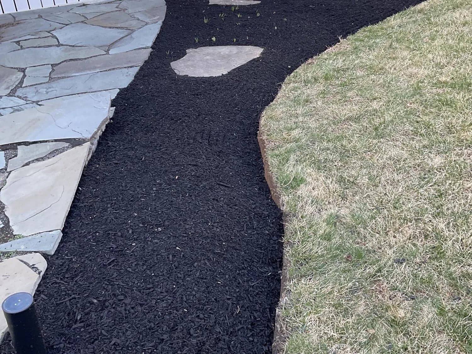 Sweeping black mulch bed edging a flagstone walkway beside a home