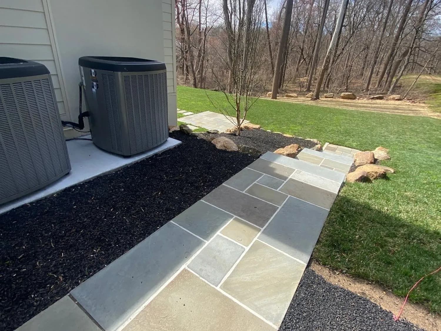 Dark mulch bed lining a bluestone flagstone walkway leading toward a wooded backyard